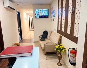 A hotel lobby with a reception desk, a sofa, a television displaying multiple screens, and a fire extinguisher.