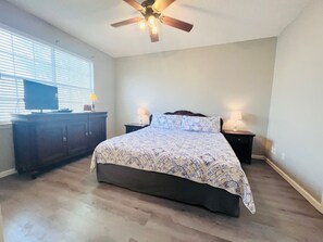 Ein Schlafzimmer mit Bett, Deckenventilator, Kommode und Fenster mit Jalousien.