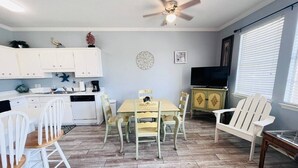 A dining area with a table and chairs, a ceiling fan, and a kitchen in the background. - 124 Seashell Cove Poinciana Place (Miramar Beach)