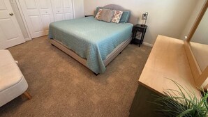 Ein Schlafzimmer mit einem Bett, einem Nachttisch, einem Sessel und einer Tür.