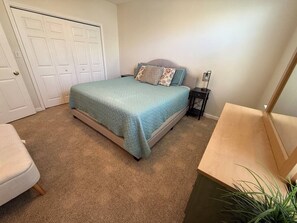 Un dormitorio con cama, mesita de noche, silla y puerta.