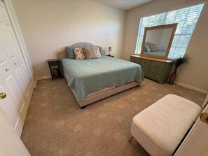 Ein Schlafzimmer mit Bett, Nachttisch, Schminktisch, Spiegel und einem Fenster mit Jalousien.