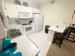 Una cocina compacta con muebles blancos, microondas, estufa, refrigerador y un pequeño comedor con mesa y sillas.