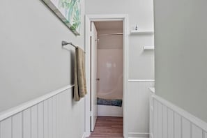 A hallway with a wooden floor, a towel hanging on a rack, and a door leading to a bathroom with a shower. - 103 Siren Cove Misty Cove (Destin)