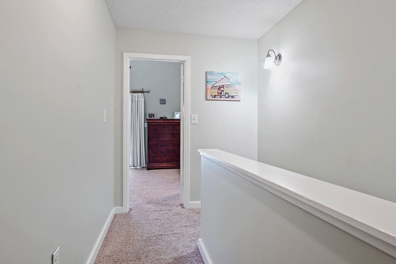 A narrow hallway with a carpeted floor, a white door leading to another room, and a wall-mounted light fixture.
