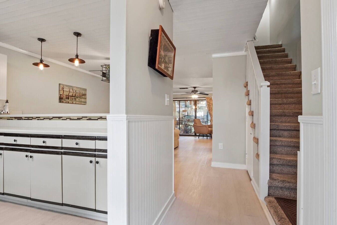 Una cocina con una isla central, un comedor con una silla y una escalera que sube a otro nivel.