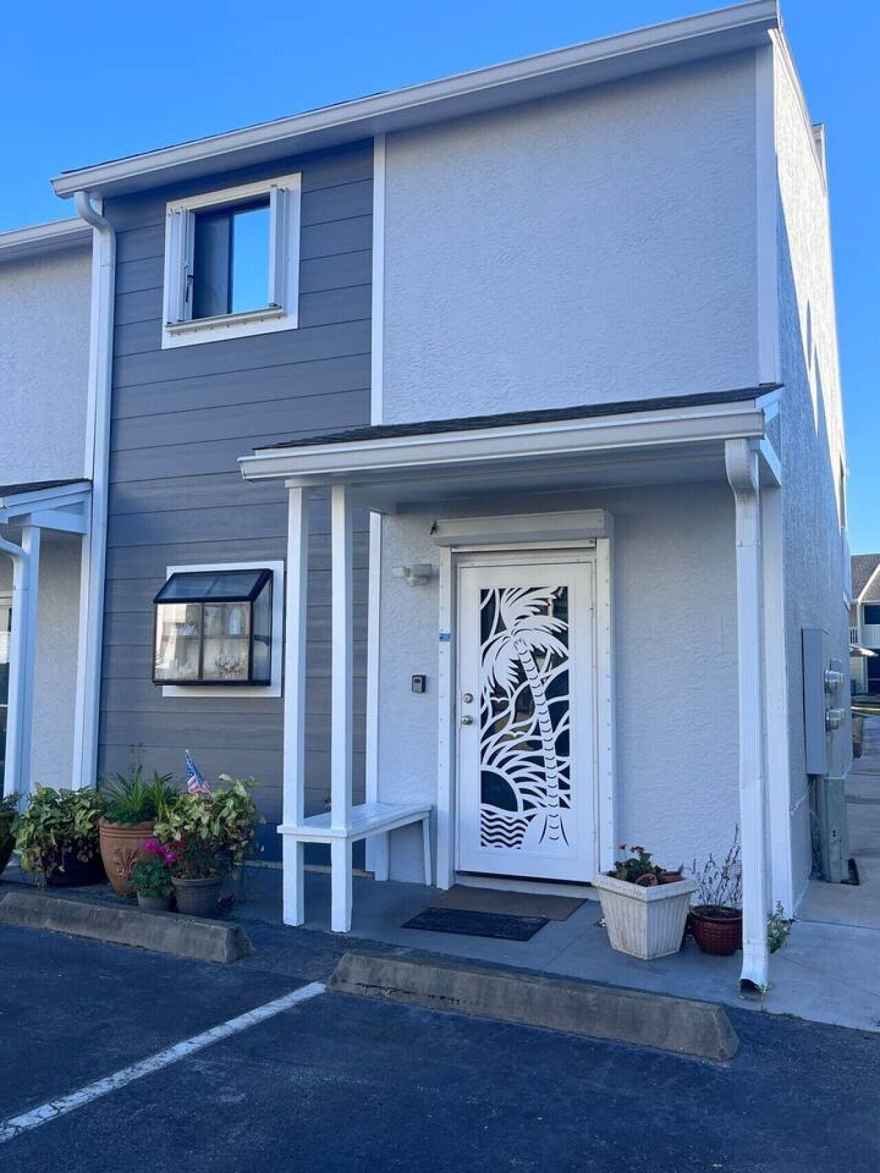 Un edificio residencial de dos pisos con fachada blanca, un porche y una puerta decorativa con diseño de palmera.