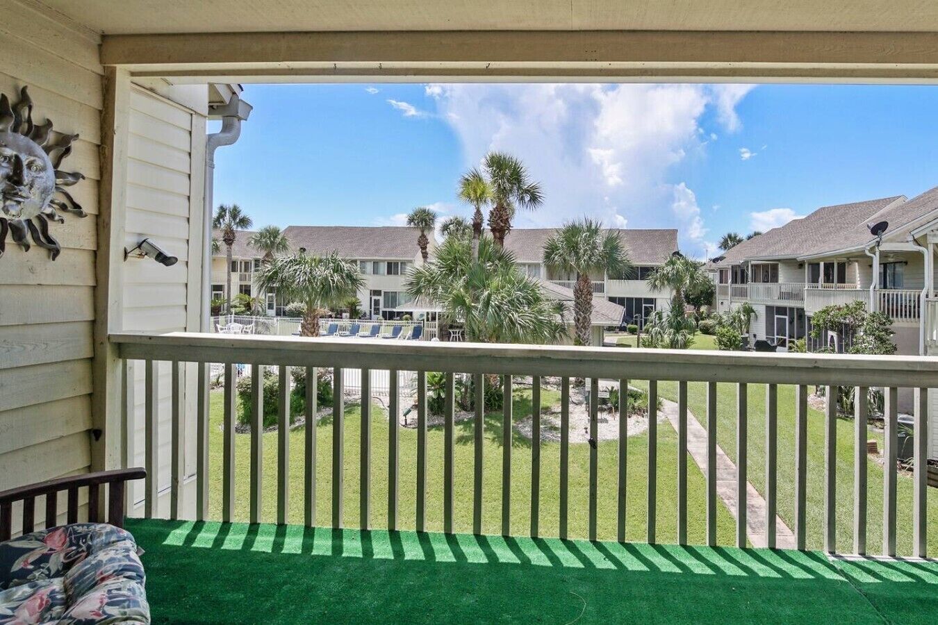 Un balcón con vista a una zona residencial, que incluye casas y palmeras.