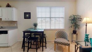 A compact kitchen with a dining table, chairs, and a window with blinds. - 214 Dolphin Cove Poinciana Place (Miramar Beach)