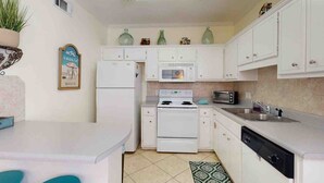 A compact kitchen with white cabinets, a microwave, a stove, and a sink. - 214 Dolphin Cove Poinciana Place (Miramar Beach)