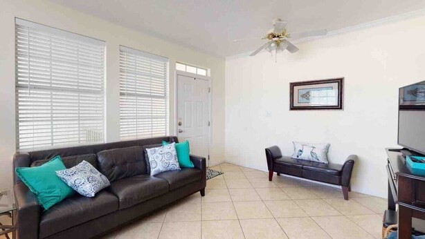 A living room with a dark brown sofa, a smaller sofa, a ceiling fan, and a television. - 214 Dolphin Cove Poinciana Place (Miramar Beach)