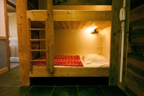 Uma cama de solteiro com escada, um cobertor vermelho estampado e um travesseiro branco.