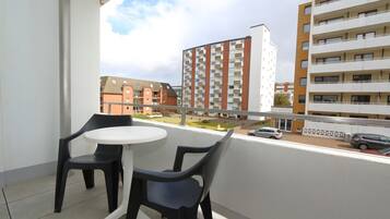 A balcony with two chairs and a small table, overlooking a residential area with multi-story buildings.