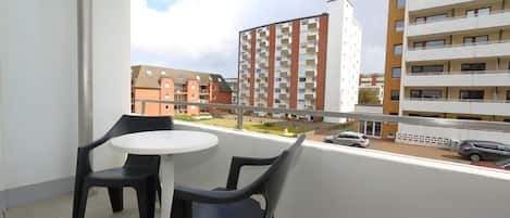 A balcony with two chairs and a small table, overlooking a residential area with multi-story buildings.