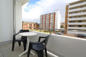 Ein Balkon mit zwei Stühlen und einem kleinen Tisch, mit Blick auf ein Wohngebiet mit mehrstöckigen Gebäuden.