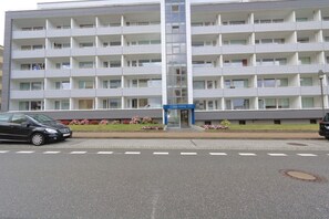 Ein mehrstöckiges Hotel mit zentralem Eingang, Balkonen auf jeder Etage und einem Parkplatz davor.