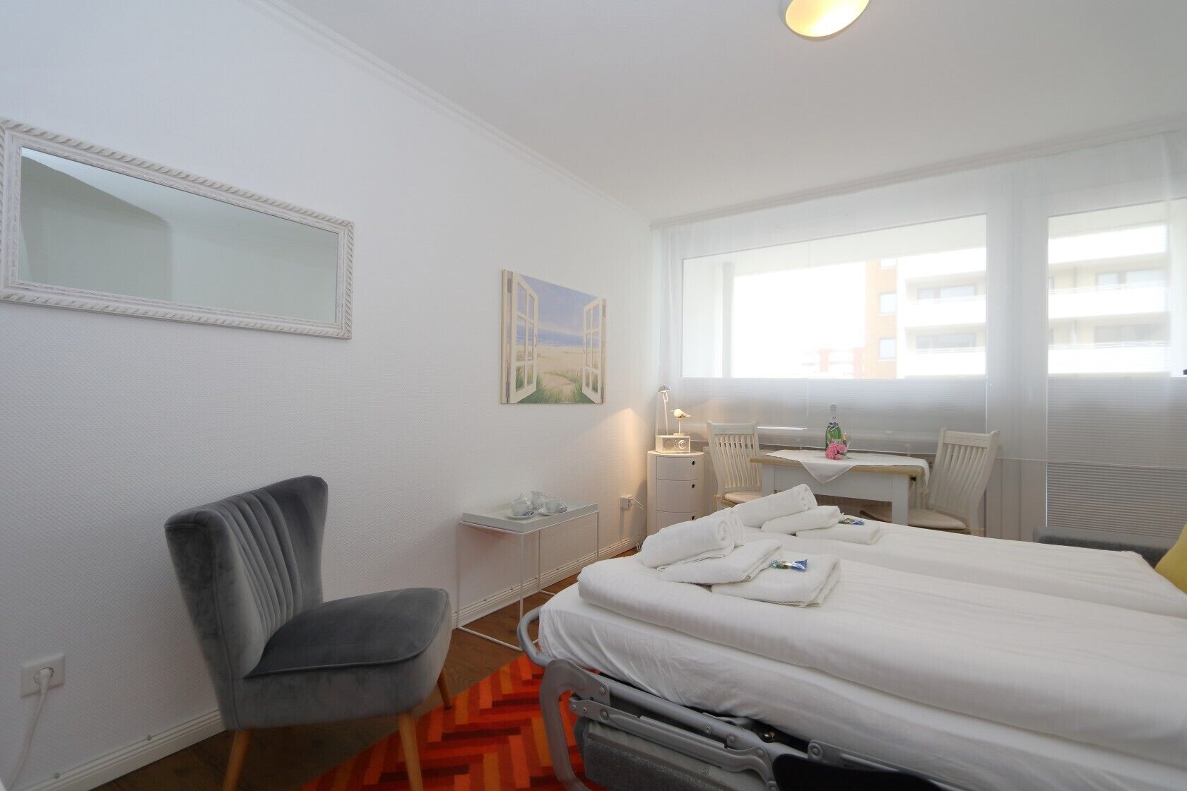 Habitación de hotel con cama, escritorio, silla, ventana y un cuadro en la pared.