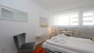 A hotel room with a bed, a desk, a chair, a window, and a painting on the wall.
