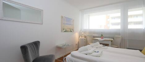 Habitación de hotel con cama, escritorio, silla, ventana y un cuadro en la pared.