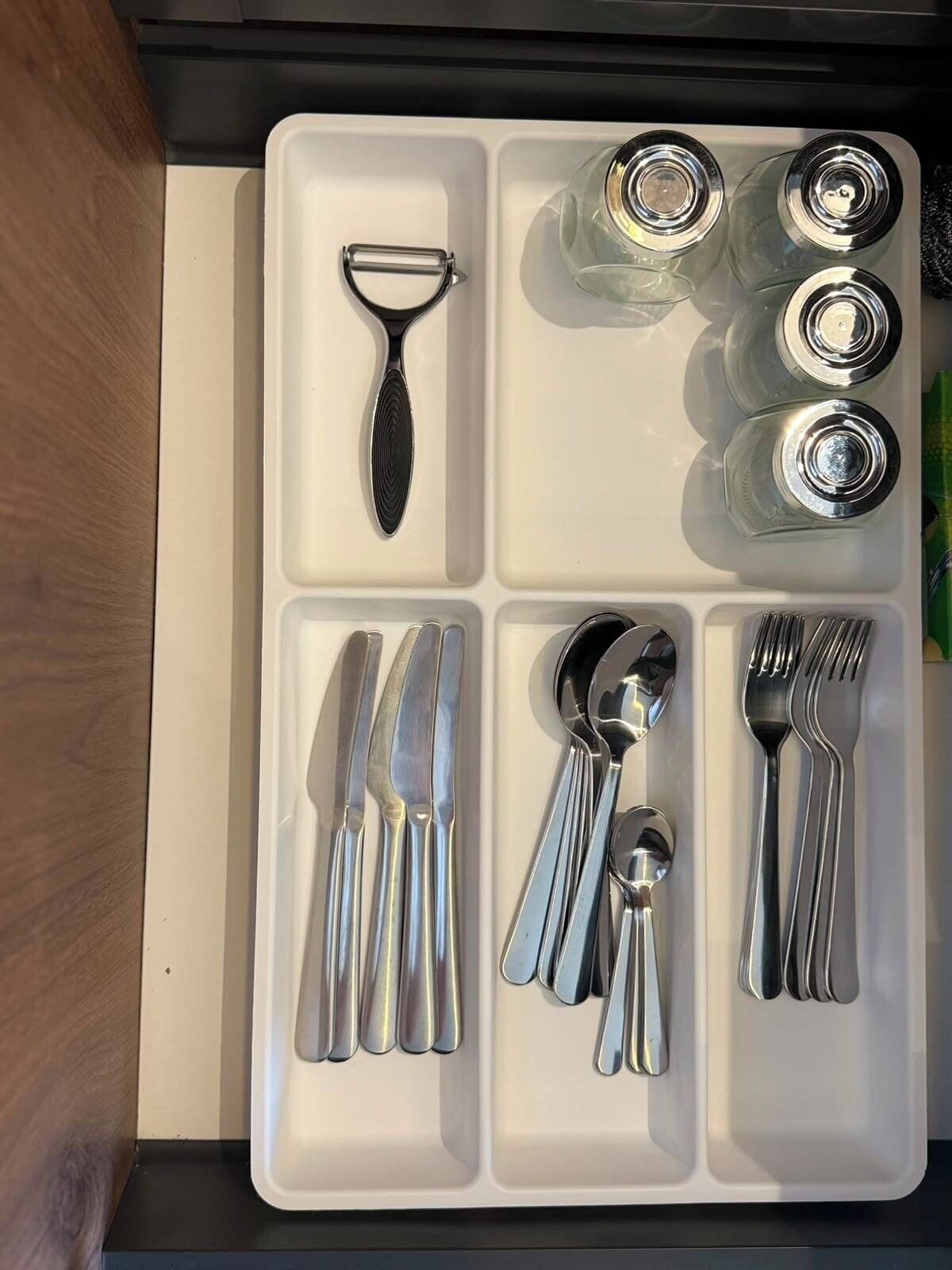 A drawer with compartments containing a spoon, fork, knife, and a grater.