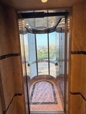 A glass elevator with a marble floor and a city view.