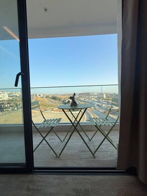 A balcony with a table and chairs, a view of a cityscape, and a clear sky.