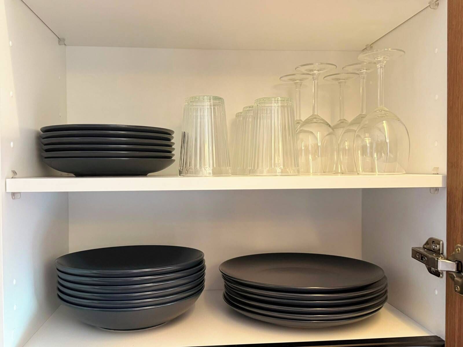 En vit hylla med svarta tallrikar och genomskinliga glas.