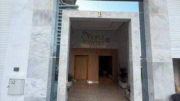 The entrance to Triple Towers with a marble facade, a wooden door, and a clear sky above.