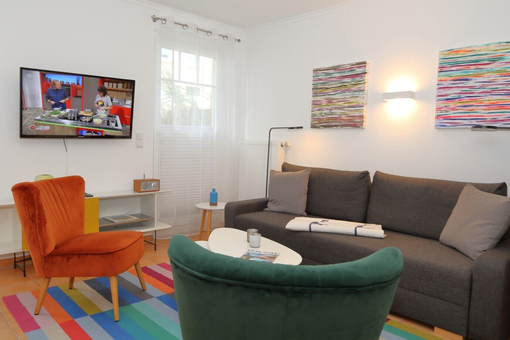 A modern living room with a sofa, armchairs, a coffee table, a TV, and a window with curtains.
