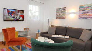 Een moderne woonkamer met een bank, fauteuils, een salontafel, een televisie en een raam met gordijnen.