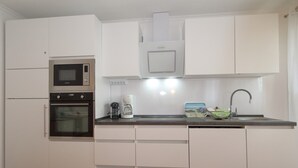 Een compacte keuken met een magnetron, oven, koffiezetapparaat en een spoelbak met een moderne kraan.