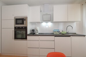 Eine kompakte Küche mit Mikrowelle, Backofen, Kaffeemaschine und Spüle mit modernem Wasserhahn.