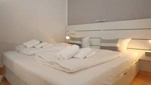 Een net opgemaakt bed met opgerolde handdoeken, een bedlampje en een hoofdbord met horizontale lijnen.