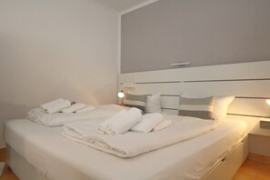 Ein ordentlich bezogenes Bett mit aufgerollten Handtüchern, einer Nachttischlampe und einem Kopfteil mit horizontalen Linien.