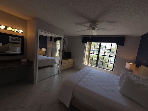 A hotel room with a bed, a TV, a ceiling fan, and a window with a view of the outside. - 1BR Villa Near Disney Pool & Resort Amenities (Kissimmee)