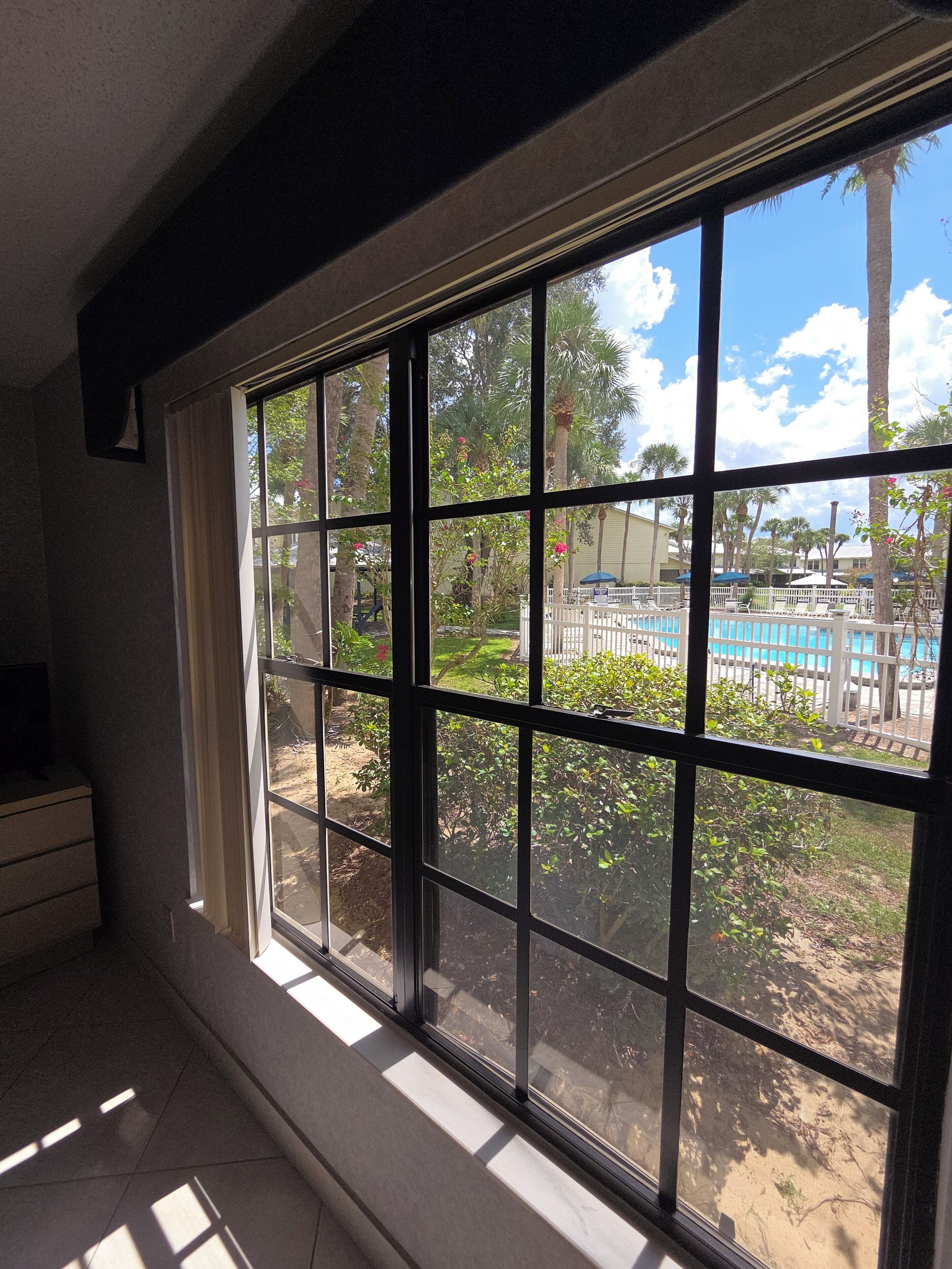 A room with a large window overlooking a pool area, a tiled floor, and a small piece of furniture on the left.