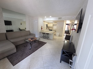 A compact living space with a sofa, a coffee table, a TV, a kitchen area, and a dining area. - 1BR Villa Near Disney Pool & Resort Amenities (Kissimmee)