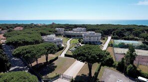 A modern building complex with multiple circular structures, surrounded by greenery and a clear view of the sea.