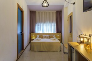A hotel room with a bed, a bedside table with a lamp, a mirror, and a window with curtains.