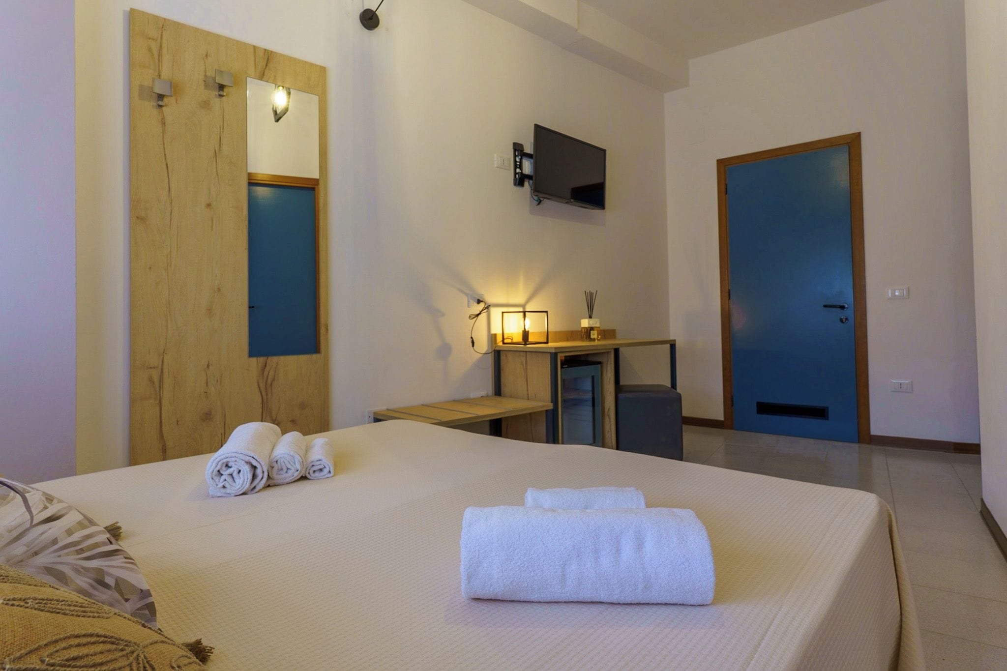 A hotel room with a bed, a desk, a TV, and a door.