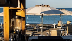 A beachside area with umbrellas and lounge chairs, a wooden structure, and a view of the sea. - Hotiday Bibbona Beach (Marina di Bibbona)