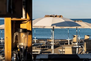 A beachside area with umbrellas and lounge chairs, a wooden structure, and a view of the sea. - Hotiday Bibbona Beach (Marina di Bibbona)