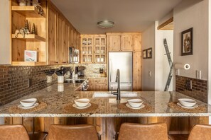 A kitchen with wooden cabinets, a stainless steel refrigerator, and a granite countertop. - Mtn Views | Free Shuttle | Fireplace (Big Sky)