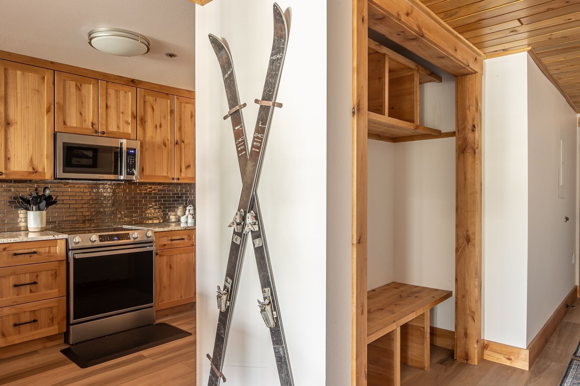 Eine Küche mit Holzausstattung, einer Mikrowelle und einem Herd. Ein Paar Ski lehnt an der Wand.