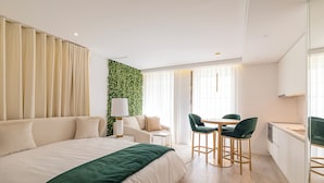 Et moderne hotelværelse med en stor seng, et skrivebord med stol, et lille bord og en væg dækket af grønne planter.