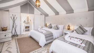 A tented accommodation with two beds, each with a swan-shaped pillow, white bedding, and patterned throw blankets.