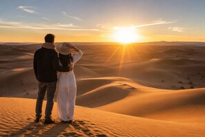 A couple standing on a sand dune with a sunset in the background. - Luxury Desert Tented  (Merzouga)
