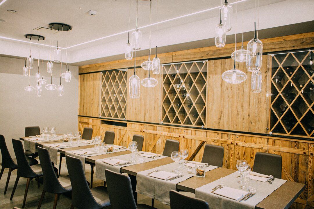 A dining area with long tables set for a meal, wooden paneling, and hanging pendant lights.