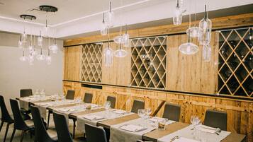 A dining area with long tables set for a meal, wooden paneling, and hanging pendant lights.