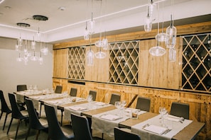 Un comedor con mesas largas dispuestas para una comida, paneles de madera y lámparas colgantes.